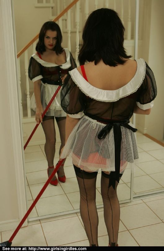 Giovane bruna in calze e uniforme da cameriera in posa davanti allo specchio
 #51291104
