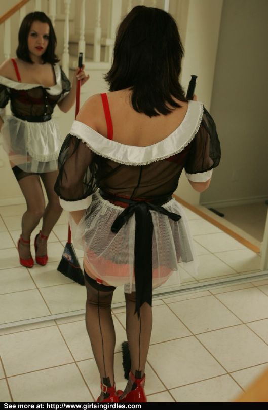 Giovane bruna in calze e uniforme da cameriera in posa davanti allo specchio
 #51291125