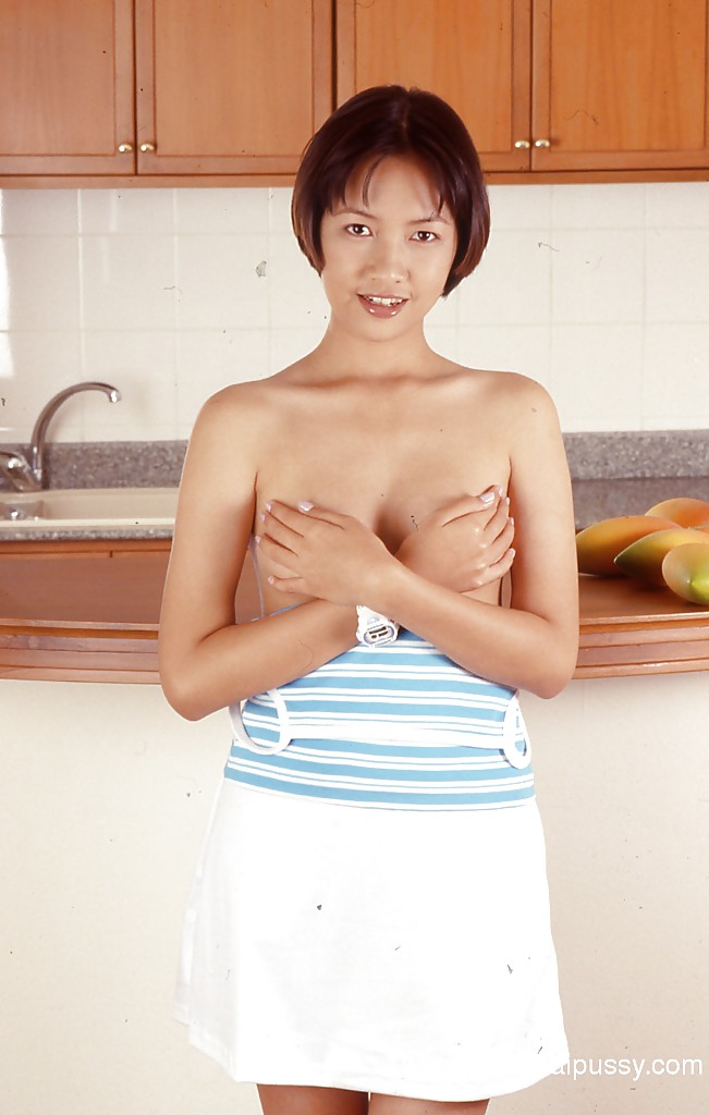 Une asiatique habillée aux petits seins pose dans la cuisine, jambes écartées.
 #51353726