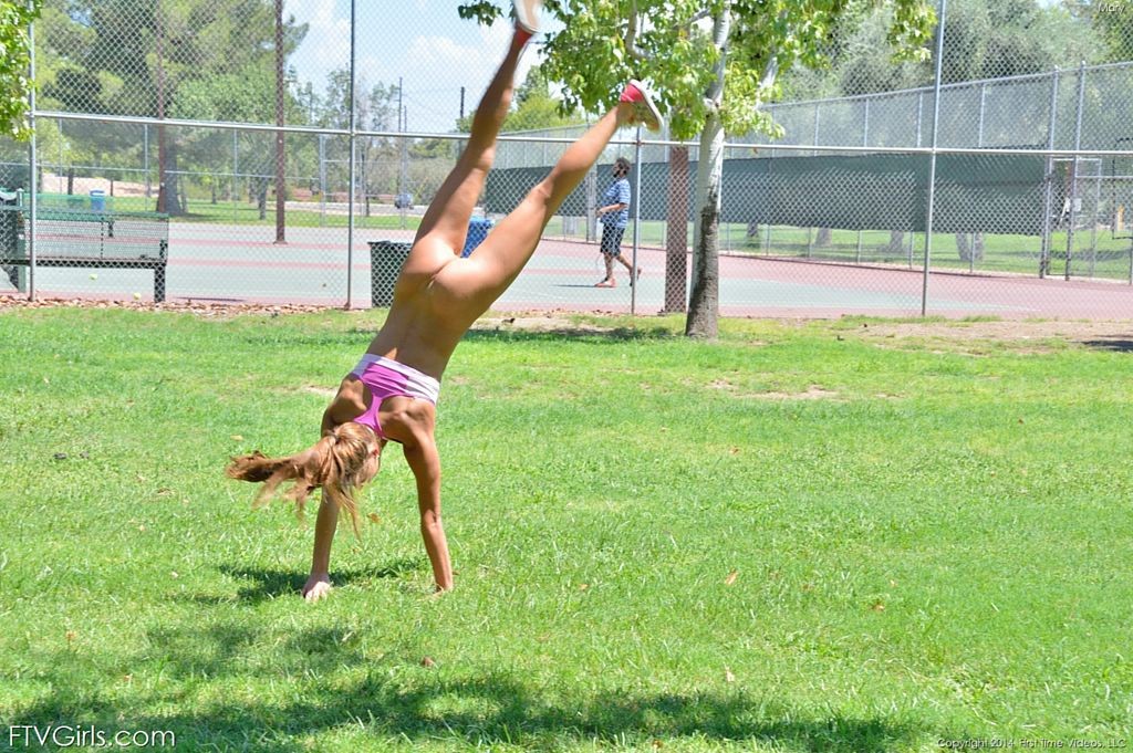 Une jolie gymnaste fait des sauts périlleux sur le court de tennis.
 #70972910