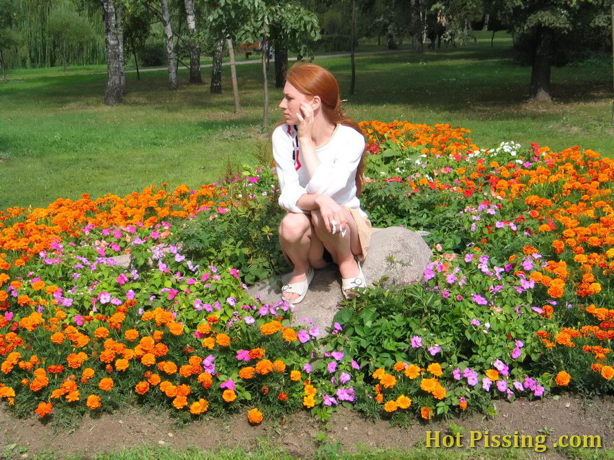 Una chica traviesa se pone en cuclillas en medio de un macizo de flores y hace pipí
 #76573000
