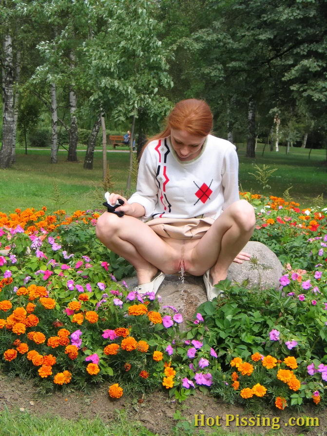 Una chica traviesa se pone en cuclillas en medio de un macizo de flores y hace pipí
 #76573014