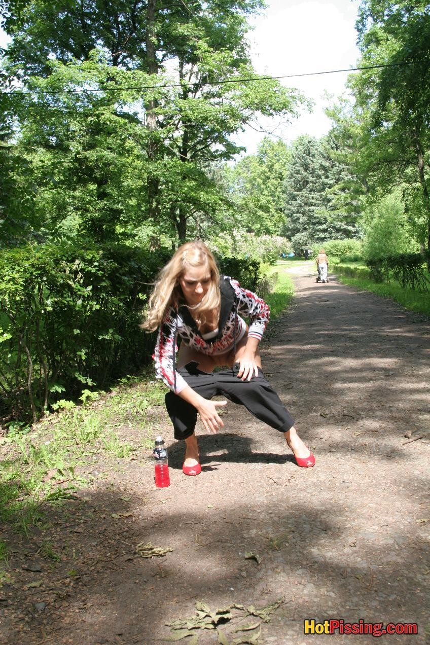 Young blondie with long hair has a piss in the middle of a park road #76521075