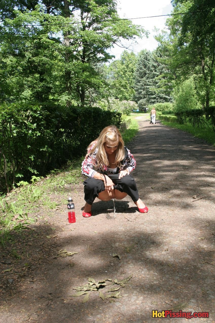 Young blondie with long hair has a piss in the middle of a park road #76521097