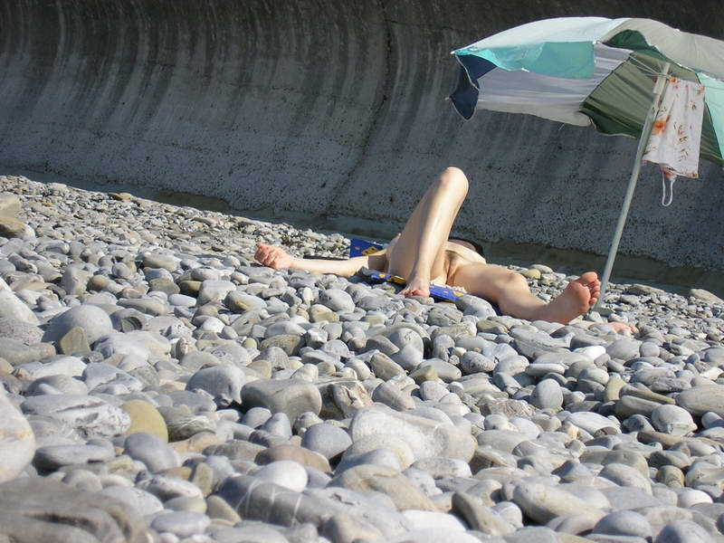 Une jeune fille aux cheveux longs se prélasse nue sur la plage.
 #72251484