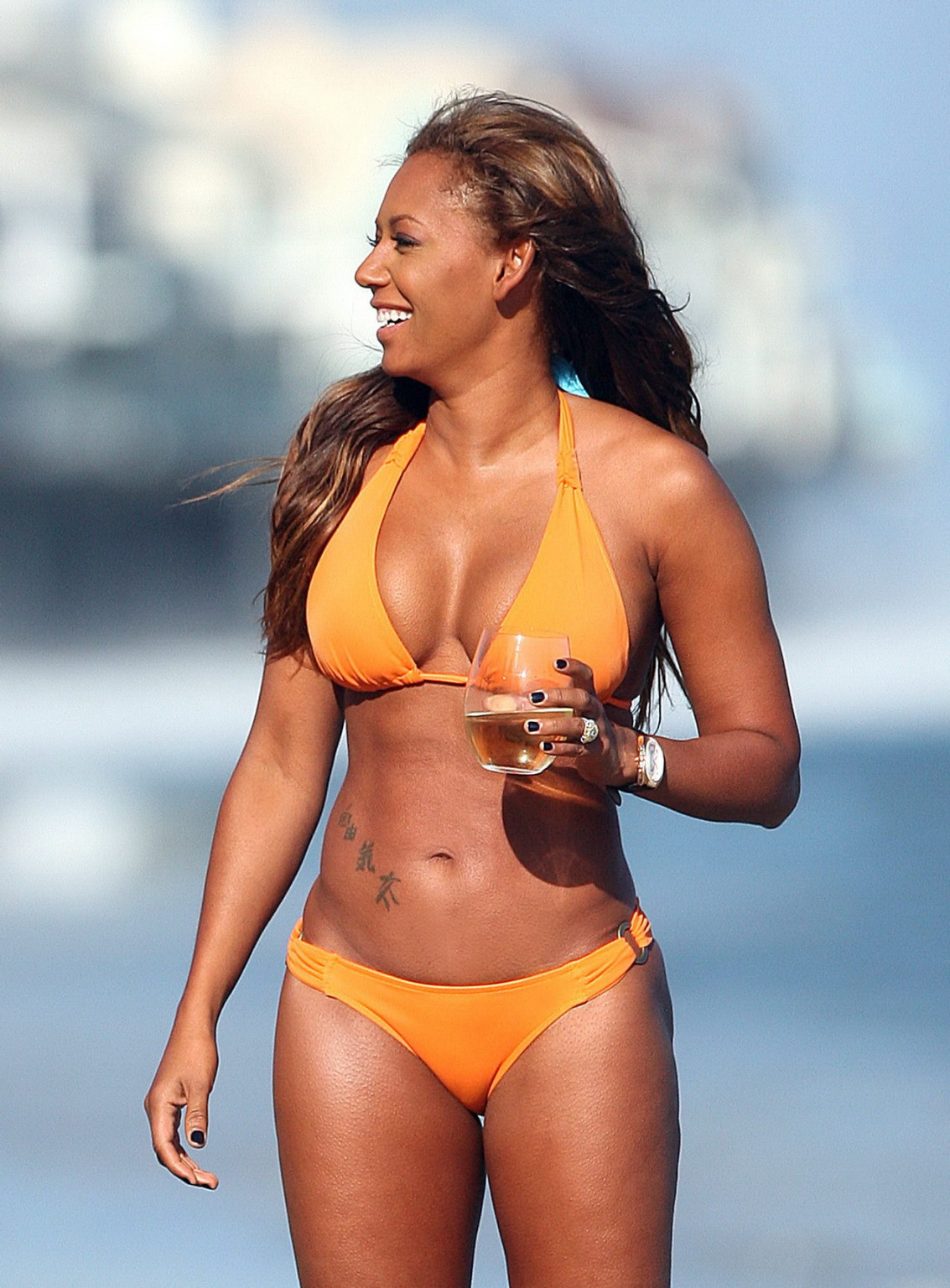 Melanie brown montre ses gros seins et ses fesses rondes dans un bikini orange très léger sur la plage.
 #75339642