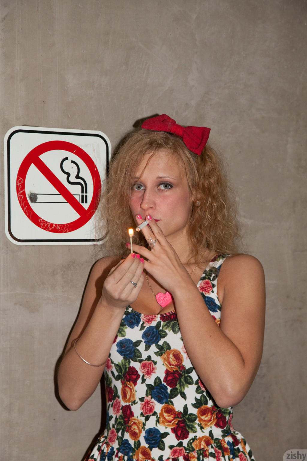 Chica rebelde con pelo rizado fumando bajo una señal de no fumar
 #67337342