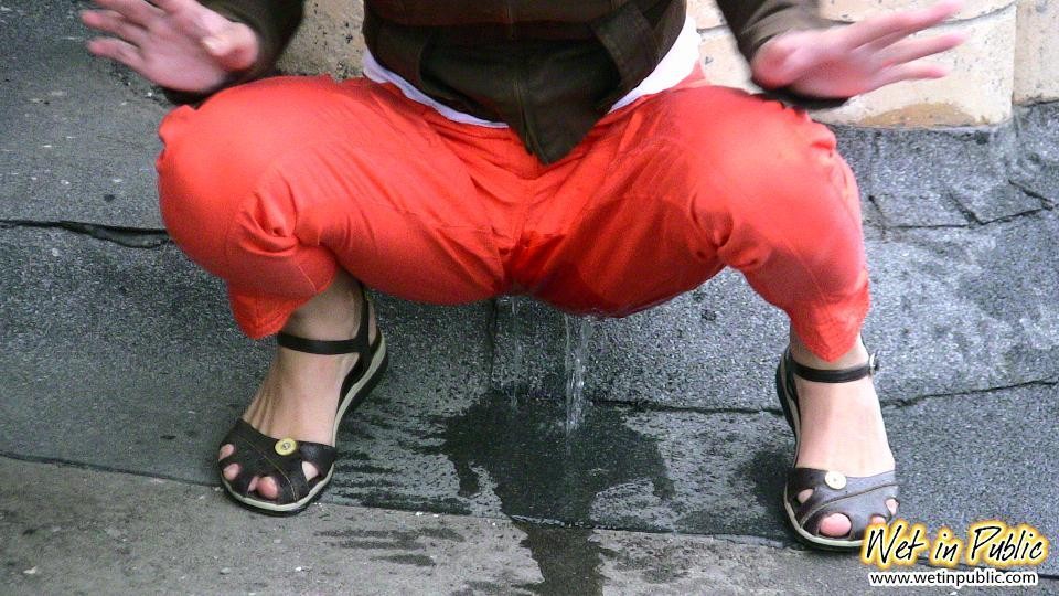 Una ragazza dai capelli corti con gli occhiali piscia nei suoi pantaloni rossi sotto gli sguardi della gente
 #73245314