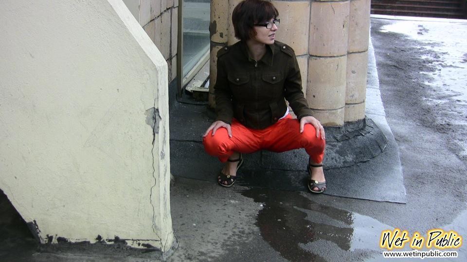 Una ragazza dai capelli corti con gli occhiali piscia nei suoi pantaloni rossi sotto gli sguardi della gente
 #73245374
