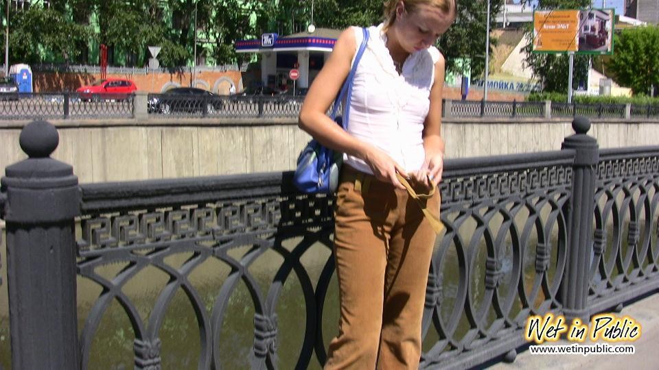 Una chica desesperada orina a través de sus pantalones de terciopelo en un terraplén del río de la ciudad
 #73238617