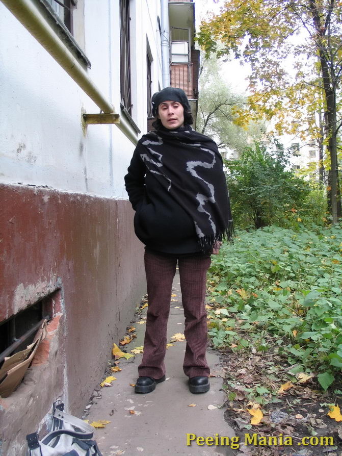 Stylishly dressed pretty woman does a leak behind a building in autumn #76571622