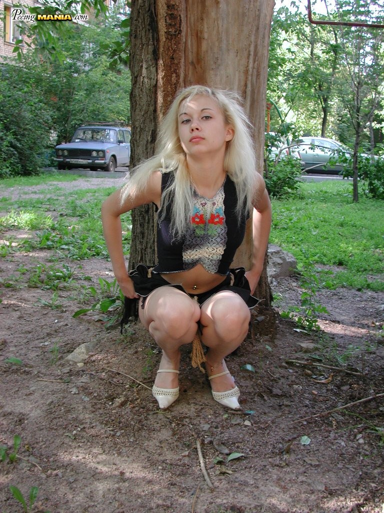 Pinkelbedürftige Blondine hockt hinter einem Baum, um sich im Park zu erleichtern
 #76566437