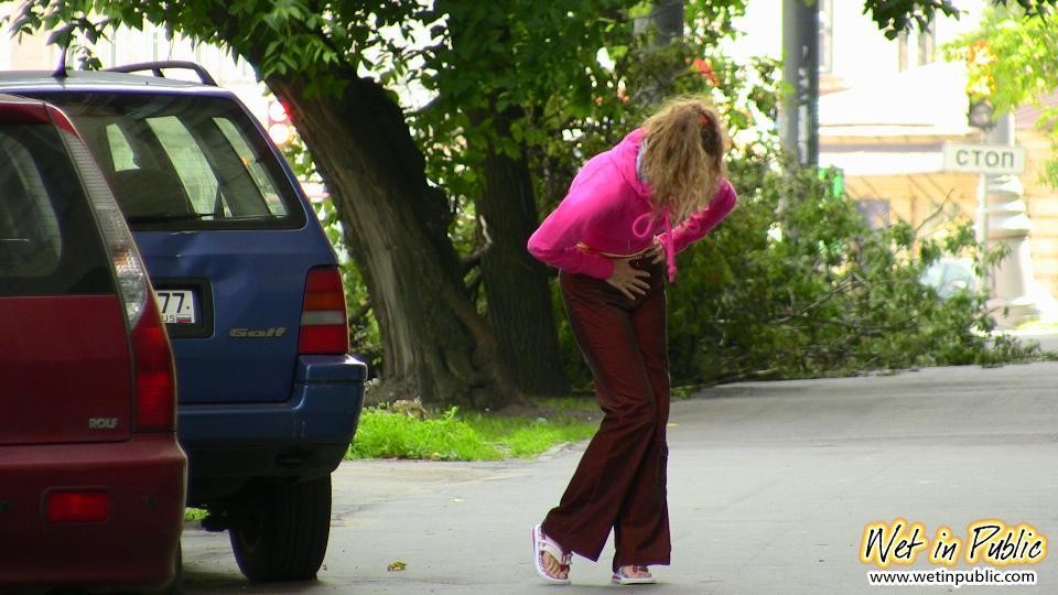 Nena desagradable moja sus pantalones carmesí detrás de un coche en el patio
 #73244390