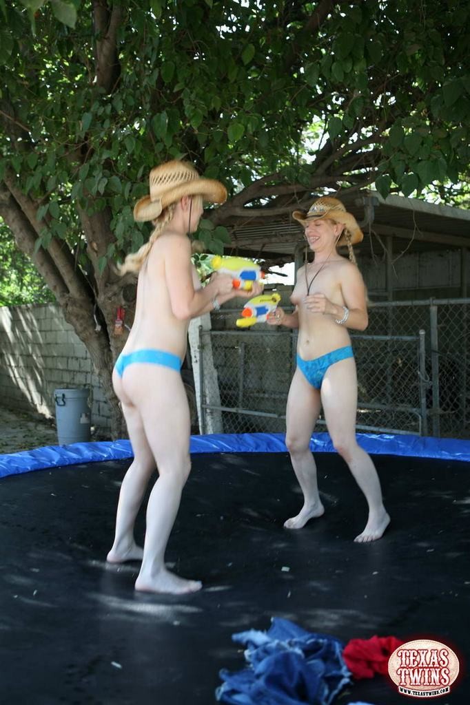 Hermanas gemelas jóvenes juegan con pistolas de agua y saltan en el trampolín
 #78657307