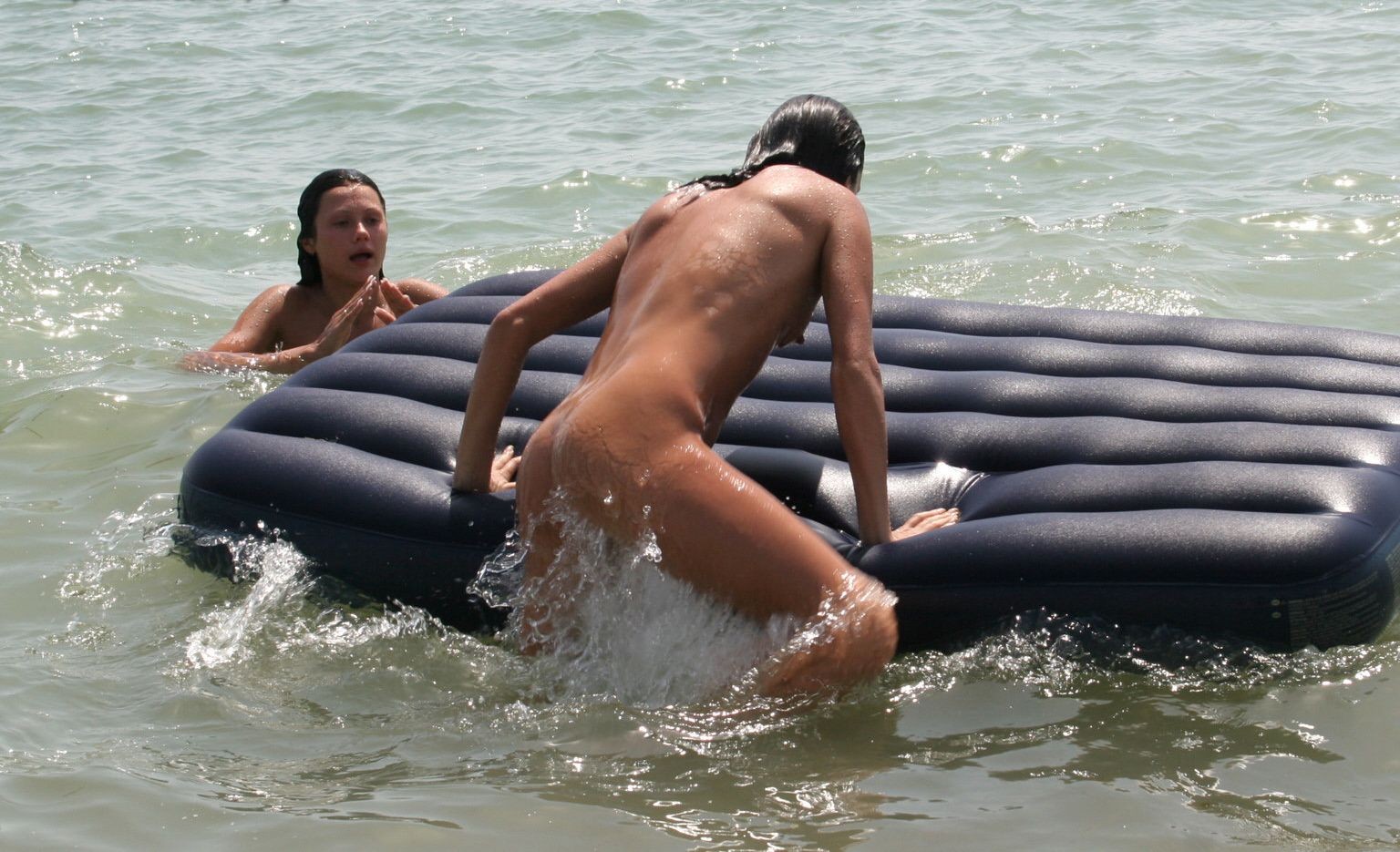 Amici nudi giocano in una spiaggia pubblica
 #72244048